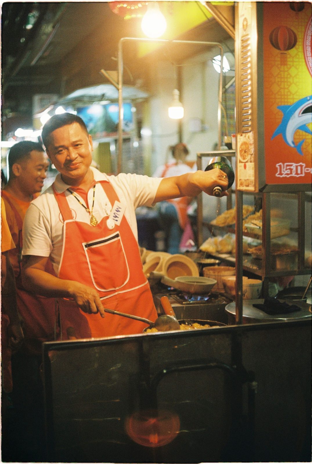 พ่อครัวร้านอาหารริมทางมองตรงมาด้วยสายตาจริงจังขณะทำอาหารหน้าเตา
