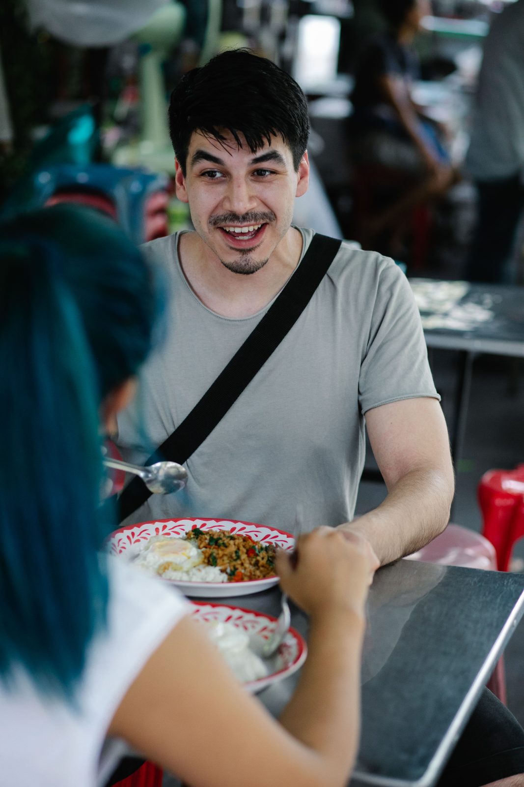 ลูกค้ายิ้มขณะนั่งกินข้าวกะเพรากับเพื่อนที่ร้านอาหารริมทาง