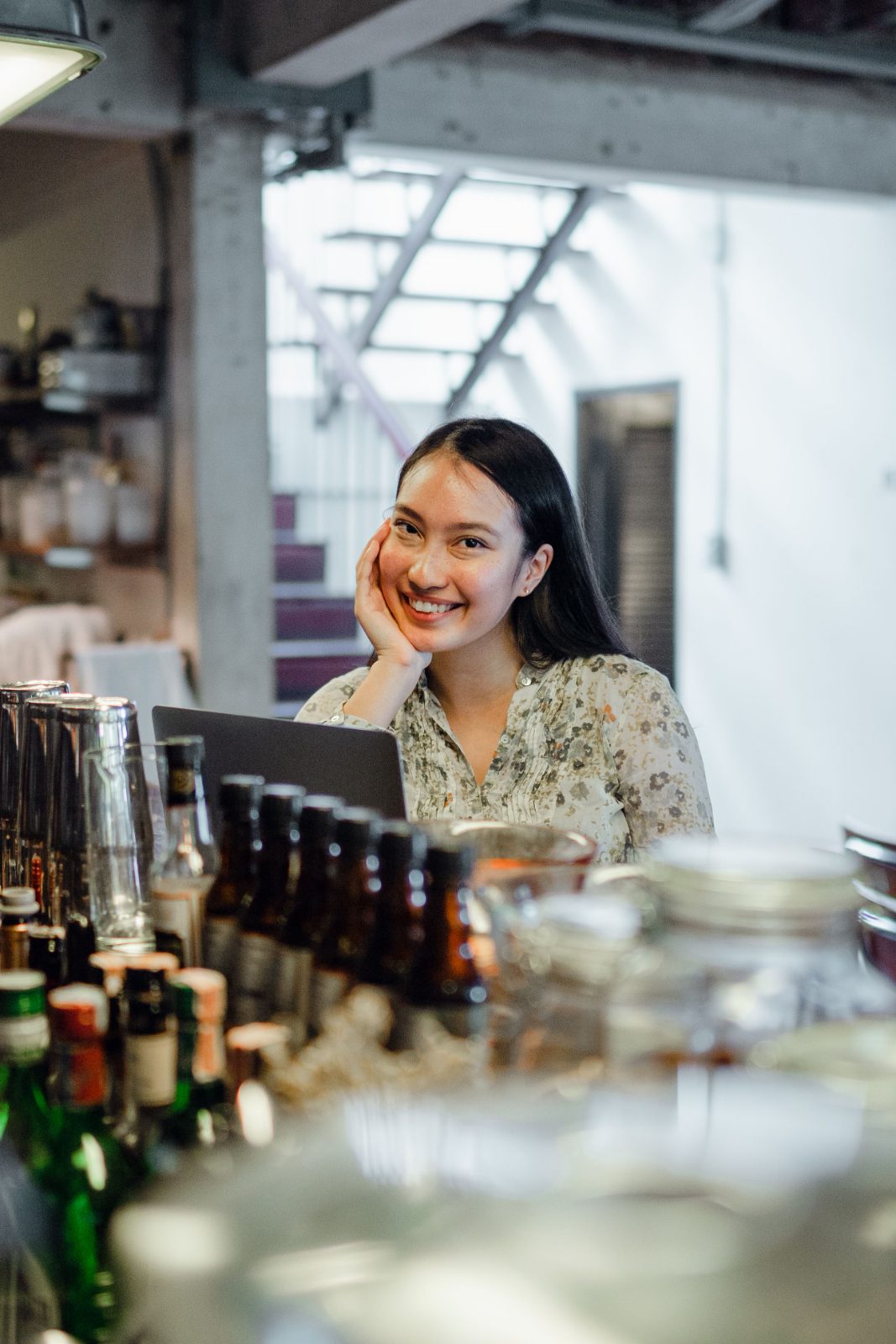 เจ้าของร้านหญิงนั่งเอามือเท้าคางหน้าแล็ปท็อปที่เคาน์เตอร์ ยิ้มบาง ๆ อย่างครุ่นคิด